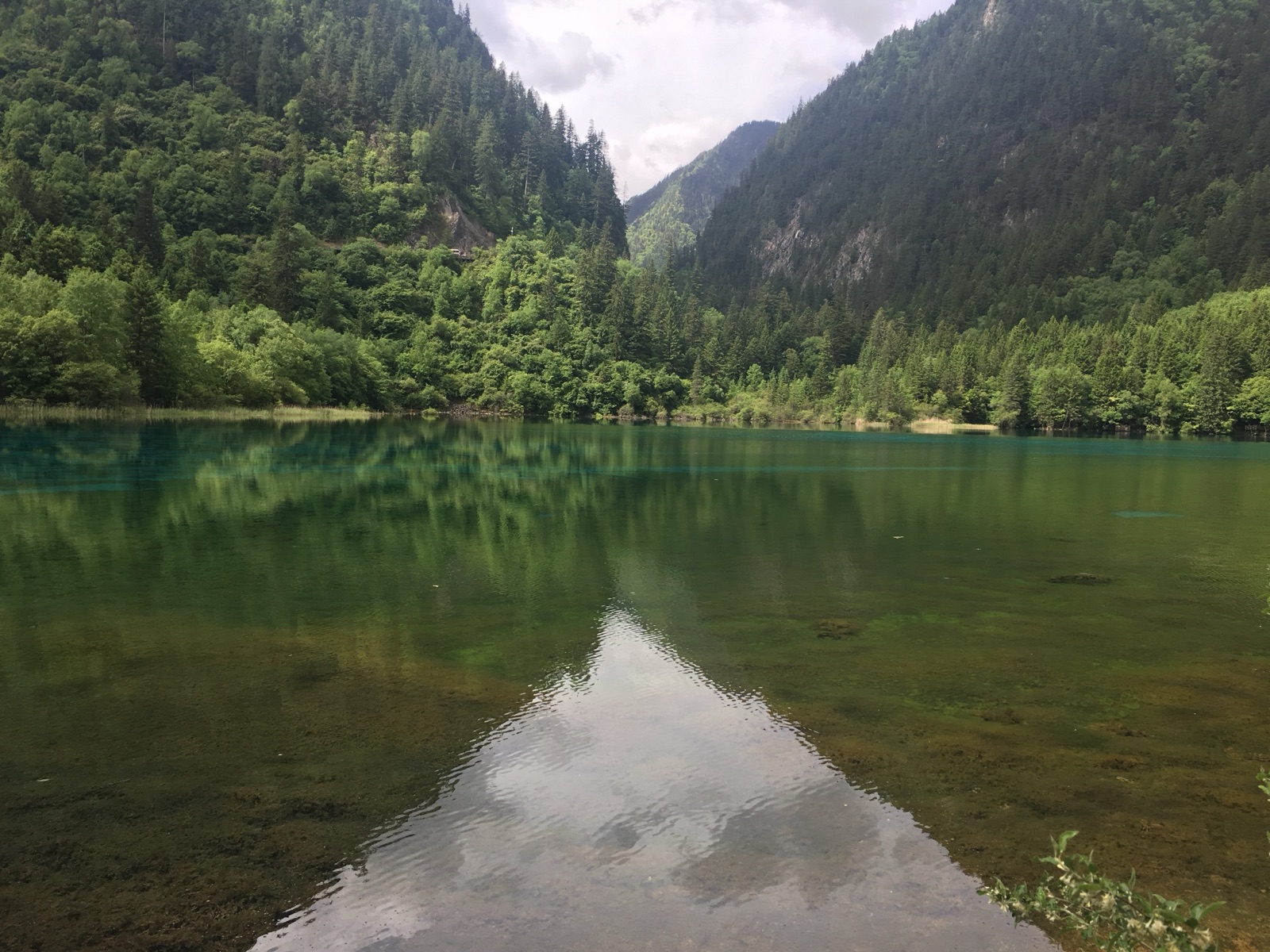A clear emerald lake reflecting forested slopes